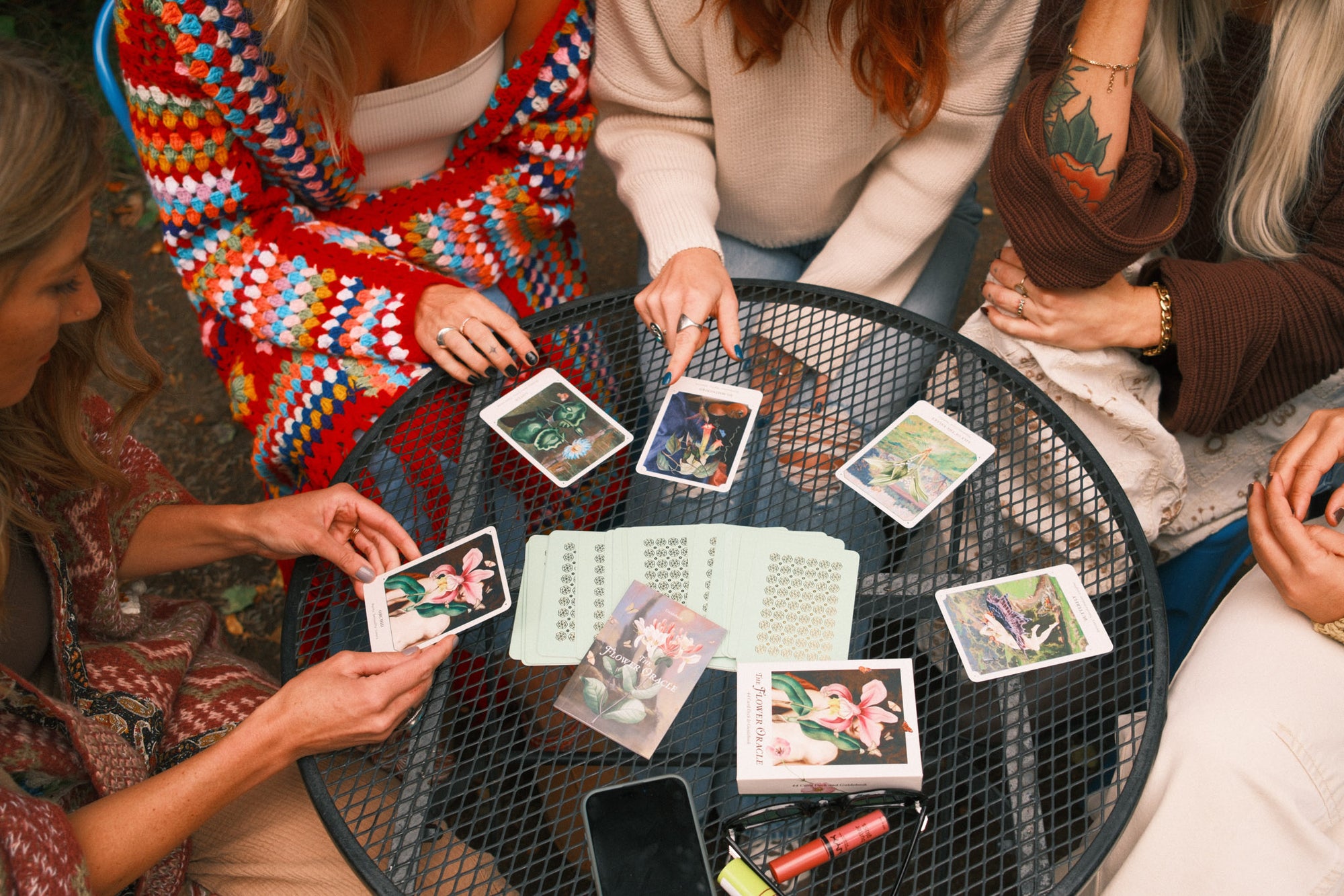 Group of people gathered around a table with tarot cards and a phone.